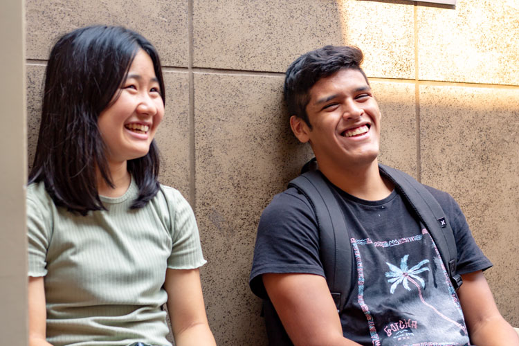 दो अंतरराष्ट्रीय अंग्रेजी छात्र हंस रहे हैं और अंग्रेजी भाषा सीखने की रणनीतियों पर चर्चा कर रहे हैं।